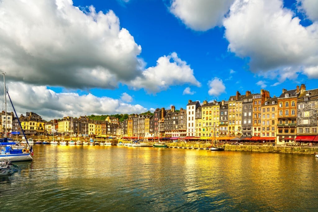 Honfleur skyline harbor and water. Normandy, France Colorful row houses along a harbor with boats docked in the water and a bright blue sky above.