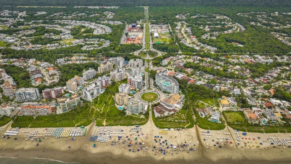 pexels-serjosoza-30117033 (1) Aerial view of a coastal city with a sandy beach lined with colorful umbrellas and lounge chairs, bordered by high-rise buildings and green parks from water-level to skyline far inland.